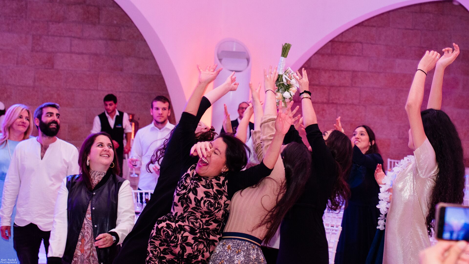 Guests reaching for the bridal bouquet at a wedding celebration