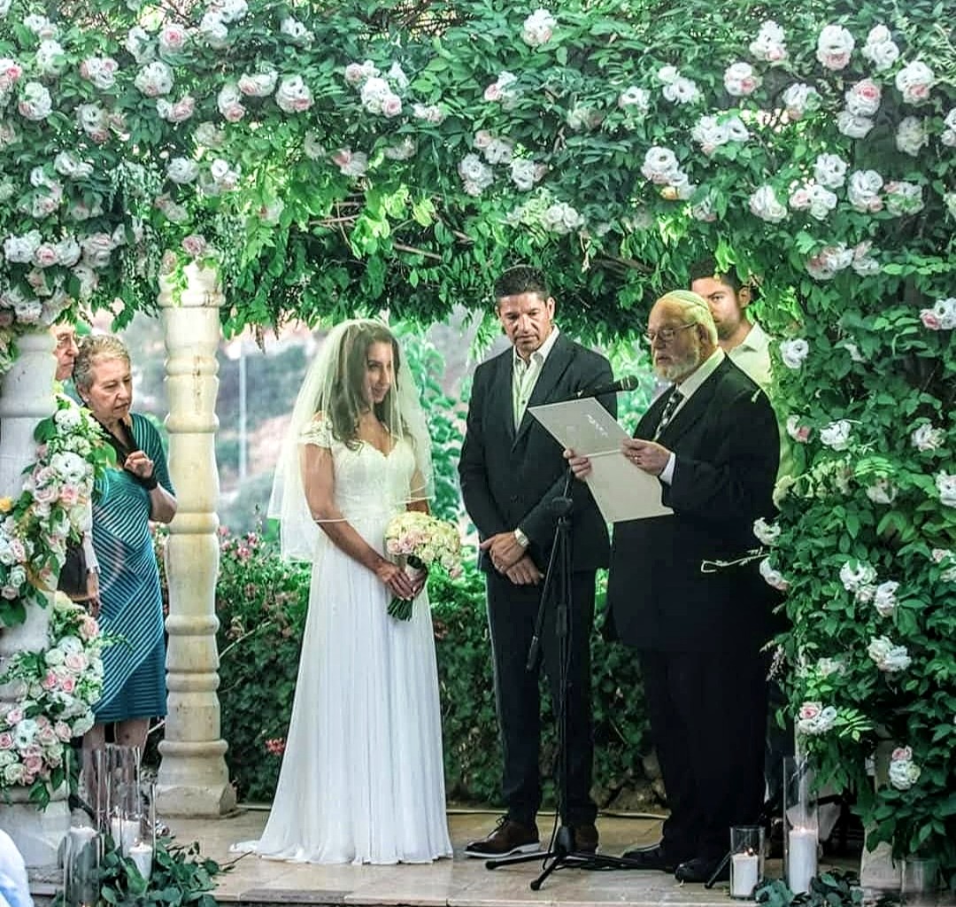 A wedding ceremony beneath a canopy of greenery and roses